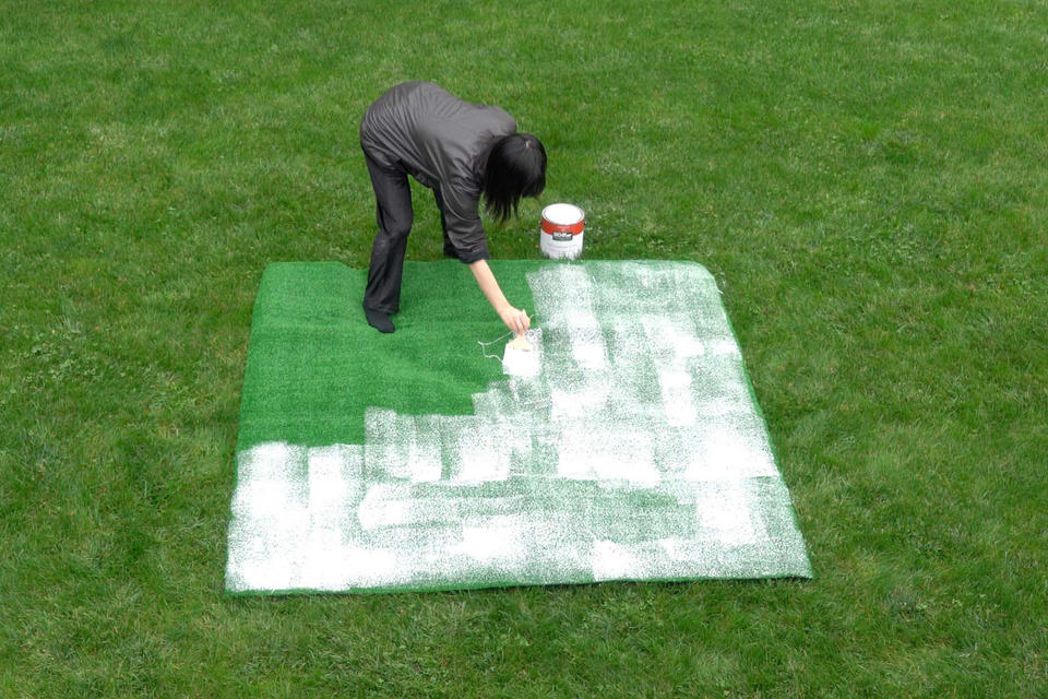 Photograph of a woman on grass painting astro turf with white house paint
