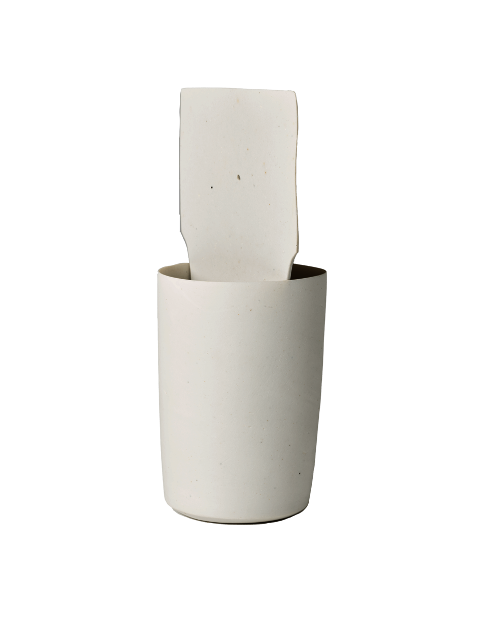 Tall, round, white cup with a white, square-shaped slice of clay on the interior of the cup.