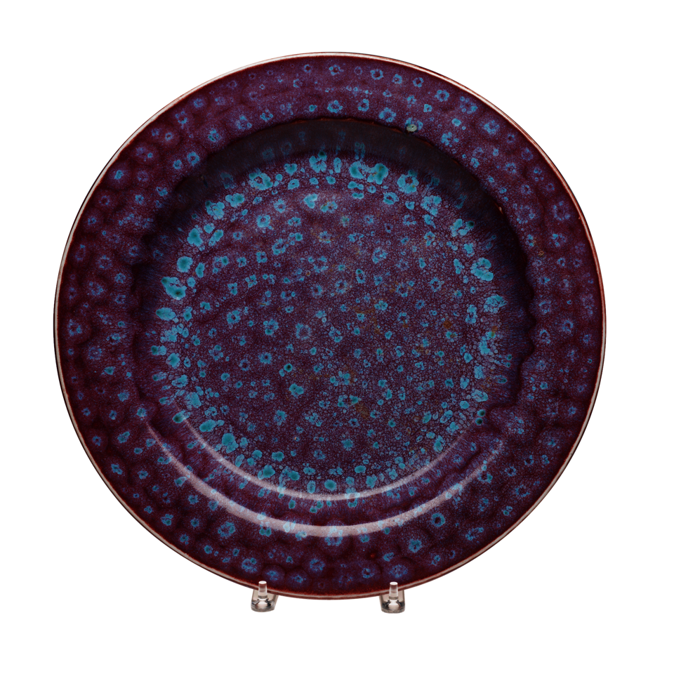 Circular plate with dark purple glaze and spots of light blue glaze in concentric circles.