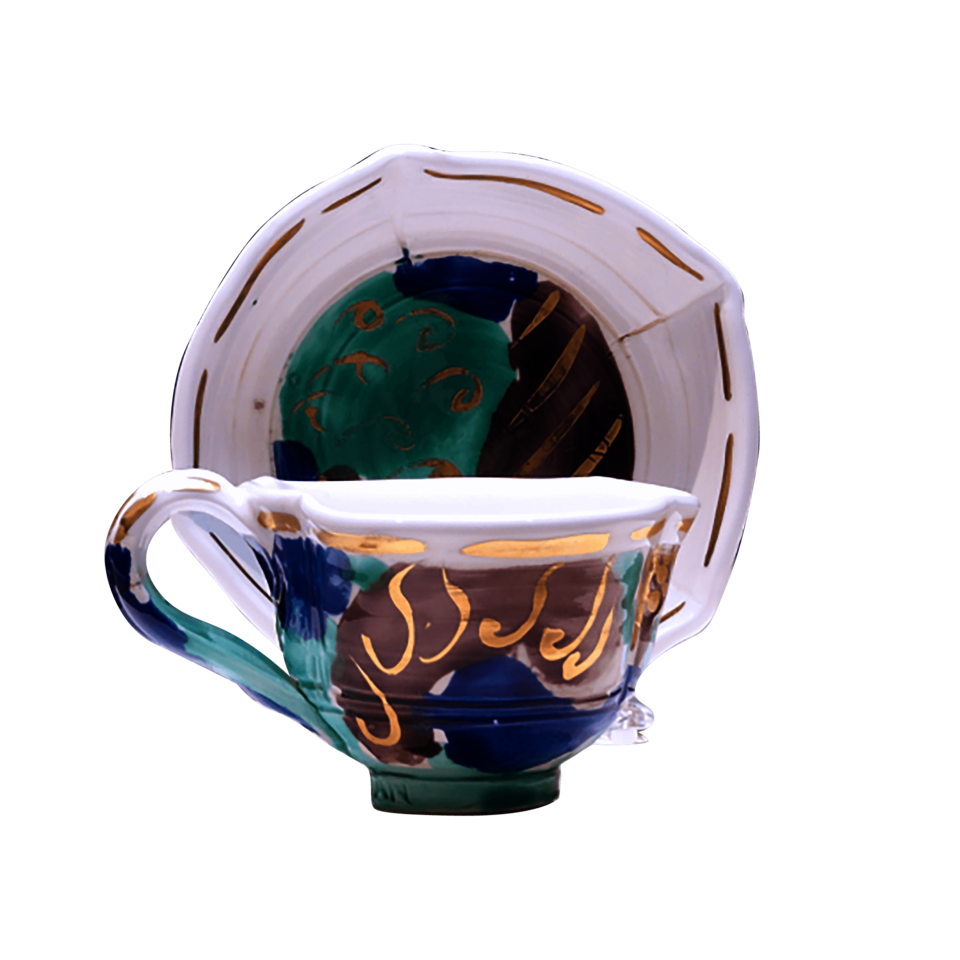 A white teacup with an upright saucer behind it. Both are covered in abstract shapes of brown, blue, and green with gold lines and squiggles.