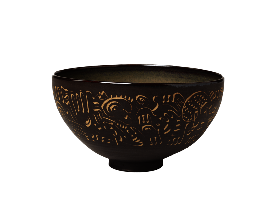 Dark brown bowl on a small, circular foot. Tan colored decorations scratched into clay covering the exterior. 