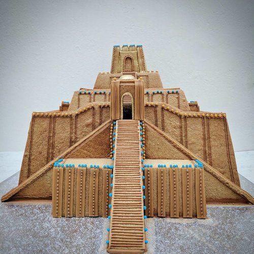 Color photograph of a gingerbread model of the Ziggurat of Ur. Light brown cookie slabs form the stepped layers and large sloping staircases, with little blue green pastilles as decorative elements.