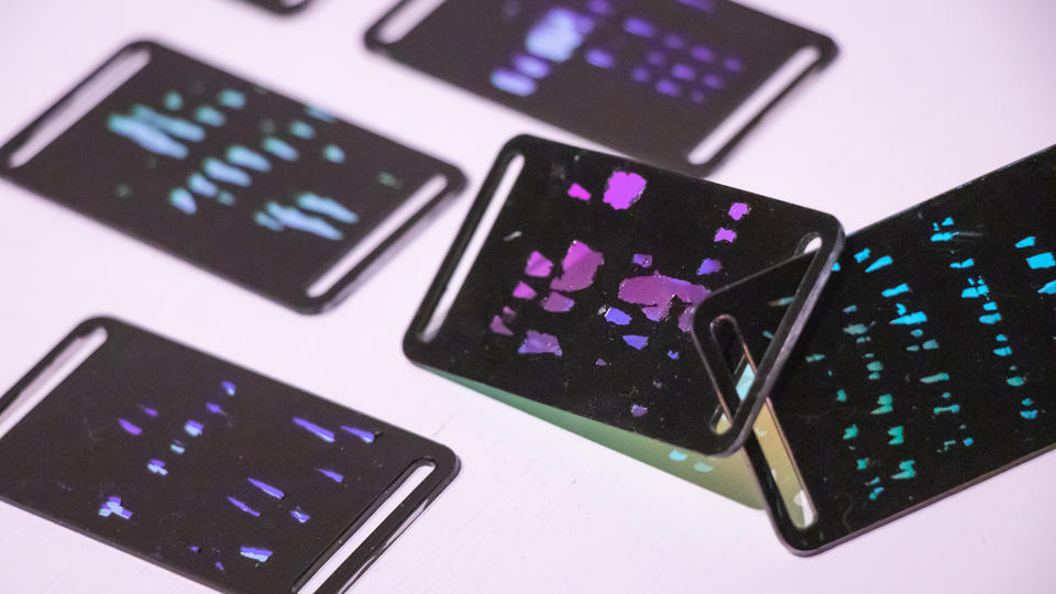 Closeup shot of 5 reaction tiles placed on a surface. the engraved parts are translucent and let light through. the angle of the light changes the transmitted and reflected colors.