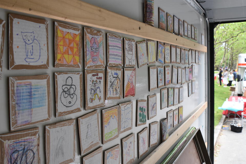 angled color photo of the interior of a Uhaul truck side; the surface is covered in small drawings done on cardboard