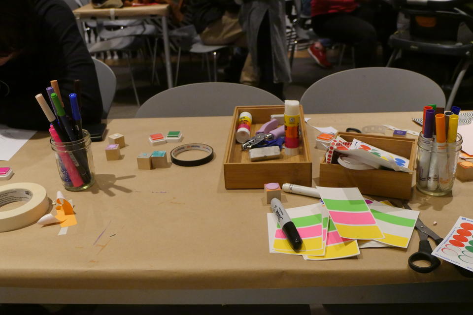 color photograph of a table covered in brown paper, topped with piles of various art supplies