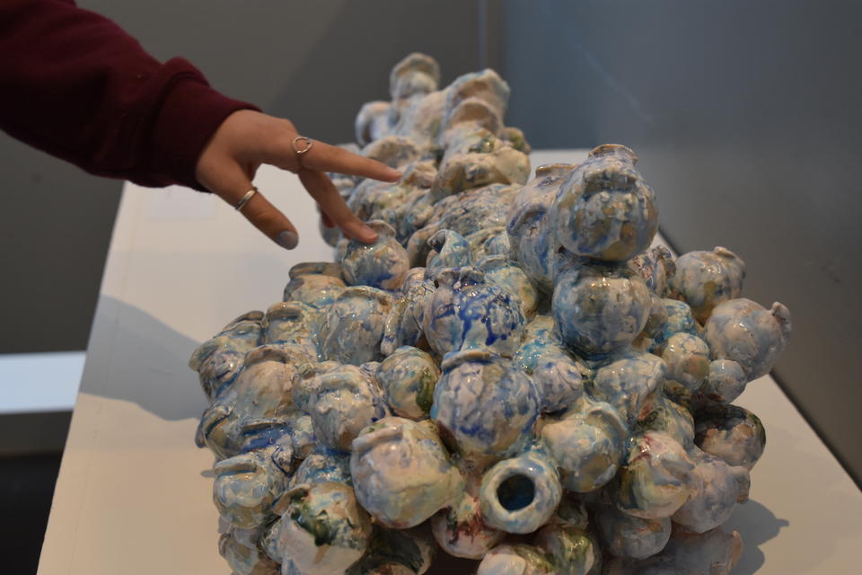 color photograph of a hand with a few rings touching a ceramic sculpture resembling a pile of small orbs