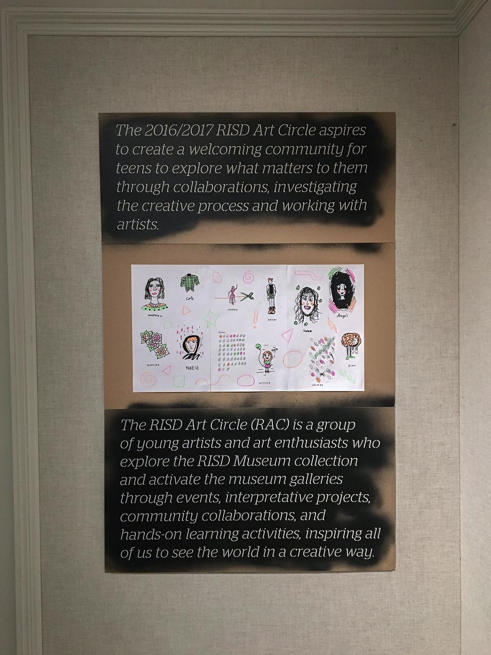 Cardboard panel with laser cut lettering with the RAC 2016/17 mission statement, and a sheet of colorful drawings.