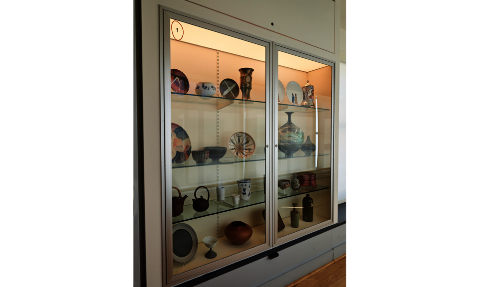 A case with four shelves is set into a wall. The shelves hold many different ceramic objects.