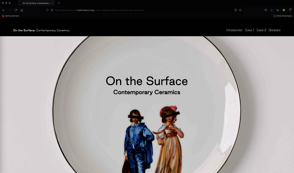 Screenshot. Text says “On the Surface: Contemporary Ceramics.” A white plate is decorated with two figures--a boy in blue and a girl in pink. Black bands cover their eyes. 