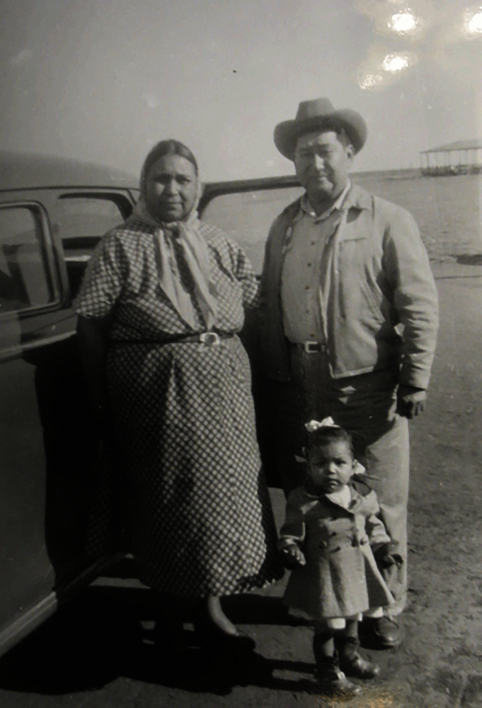 Black and white photo of an older couple with a young child, standing next to a car.