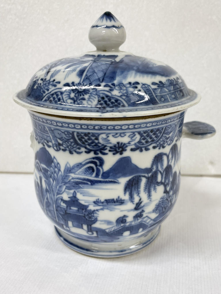 A white ceramic sugar bowl with flat handles and lid, the decorations are architectural and floral. 