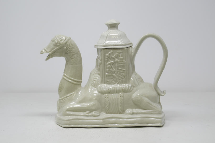 A completely white earthenware camel shaped teapot with a hexagonal lid.