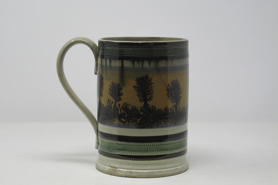 An earthenware tankard that has white, blue, orange, green, and dark brown/black glaze vertical decorations.