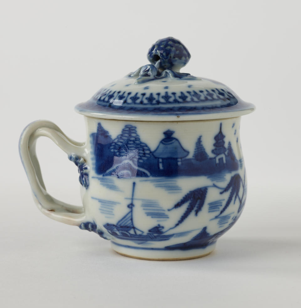 A porcelain covered cup with a sculptural swirled handle and blue architectural, floral, and scenic decorations.