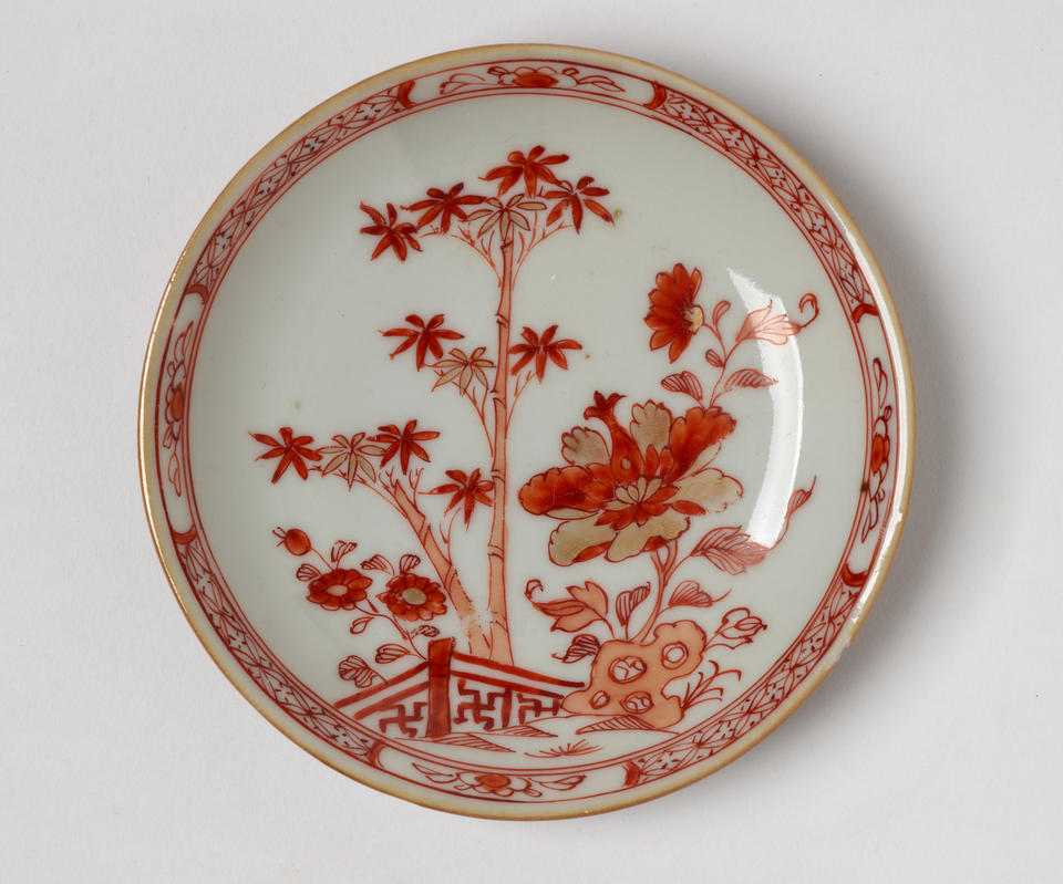 A porcelain teacup with iron-red and gold floral, structural, and abstract decorations. 