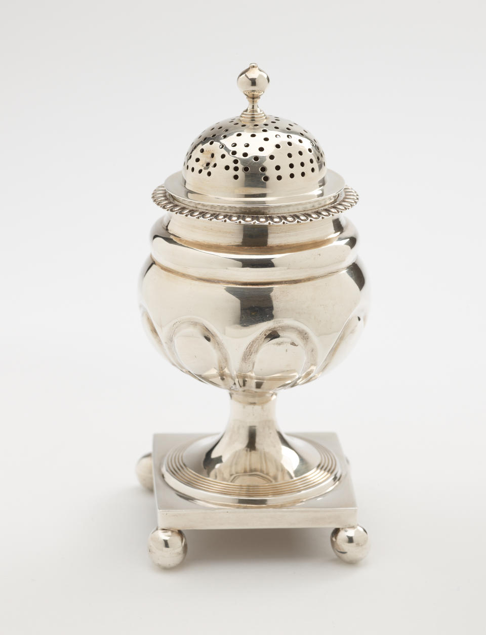 A silver caster with a square foot with small balls in each corner, the lid is perforated. 