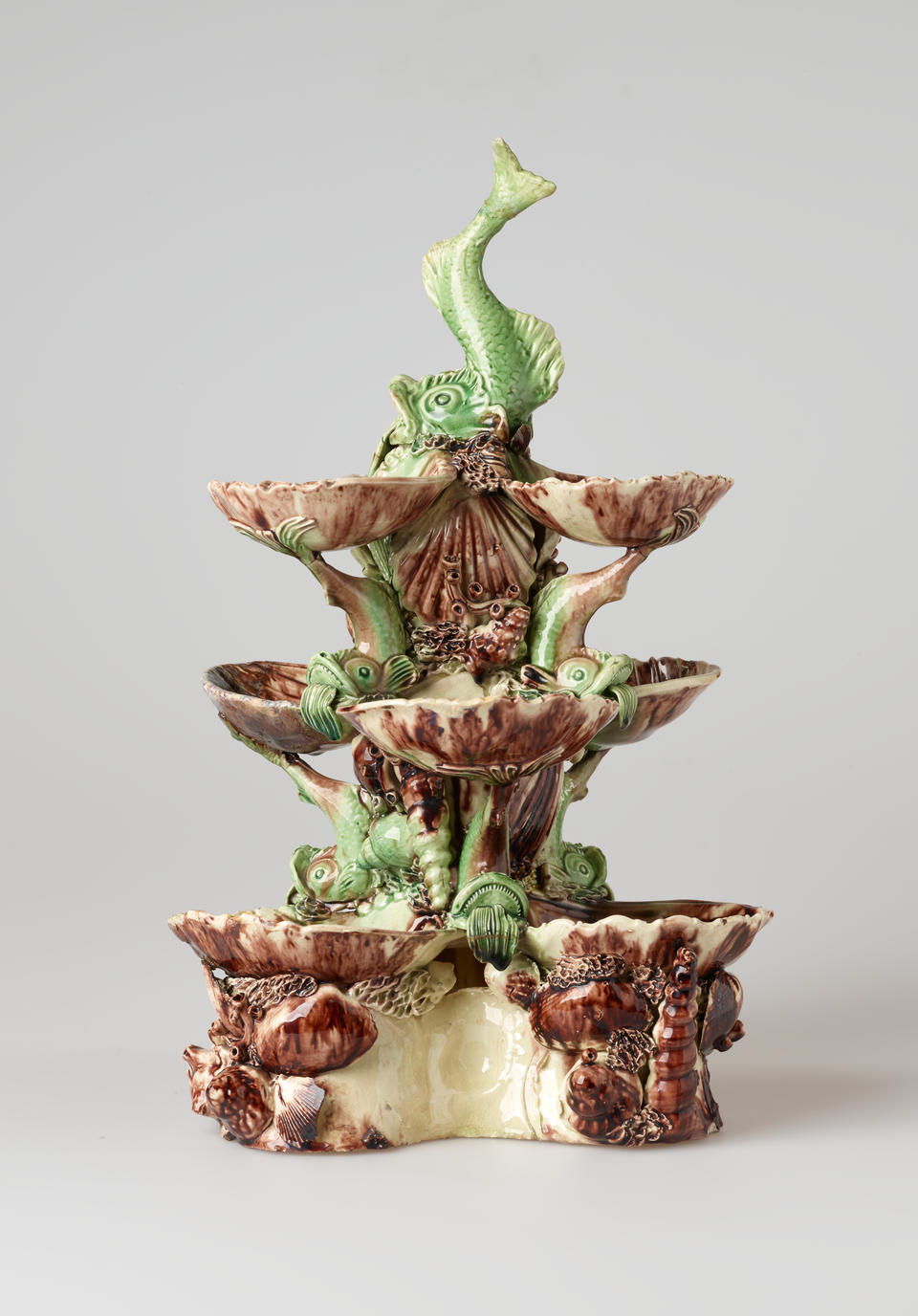 An elaborate sculptural three tiered sweetmeat dish that is dark purple, green, and cream glaze with floral decorations as well as sculpted fish decorations.