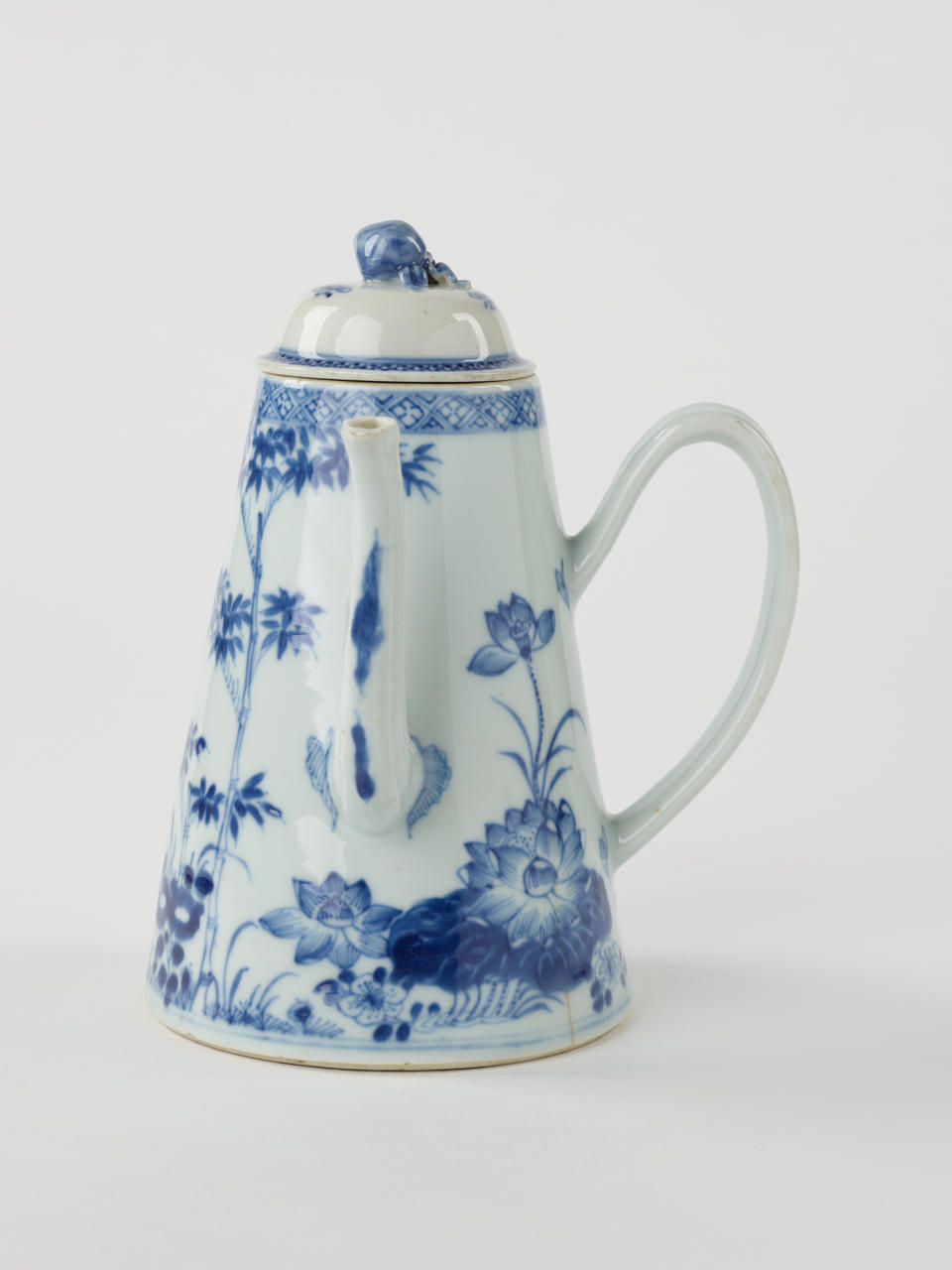 A white and blue teapot with floral decorations, a lid with a small semi spherical finial, spout, and a handle which is located approximately 90 degrees from the spout.