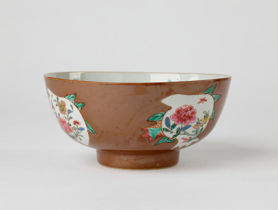 A white and brown ceramic bowl with green, yellow, and pink floral decorations with a short, small foot.