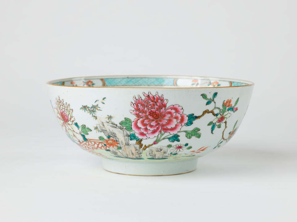 A white ceramic punch bowl with a short foot and teal, green, pink, and red floral decorations along the body and inside of the vessel. 