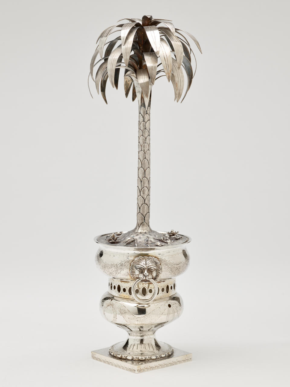 Silver sculpture in the shape of a palm tree, sitting inside an urn. 