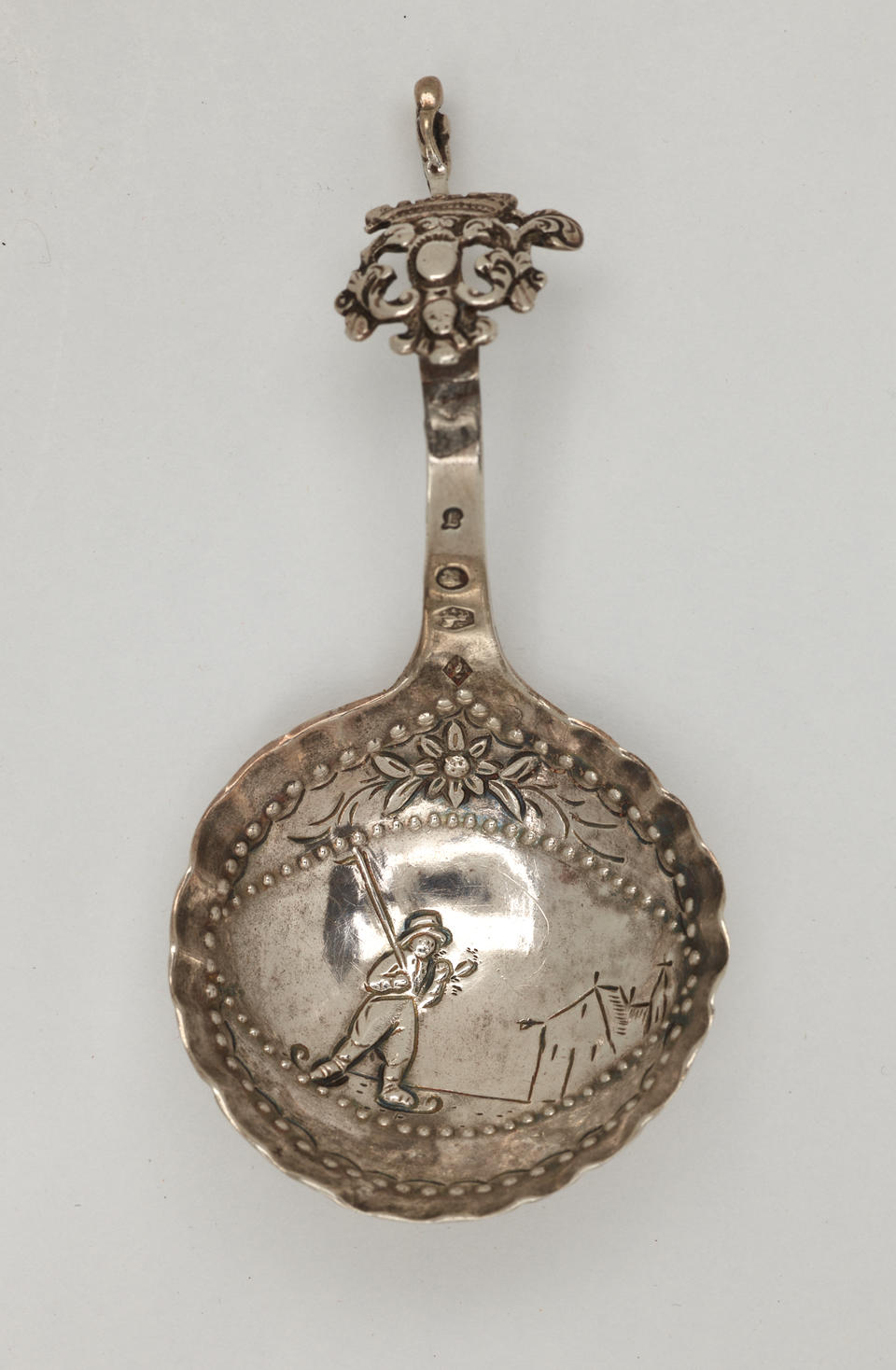 A silver caddy spoon with figurative and sculptural elements.