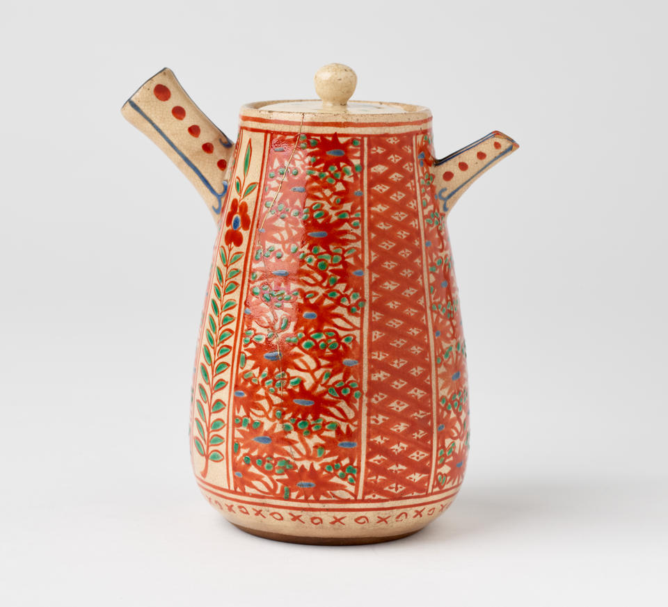 A stoneware teapot with enamel floral and abstract decorative motifs that are red, green, and blue. 