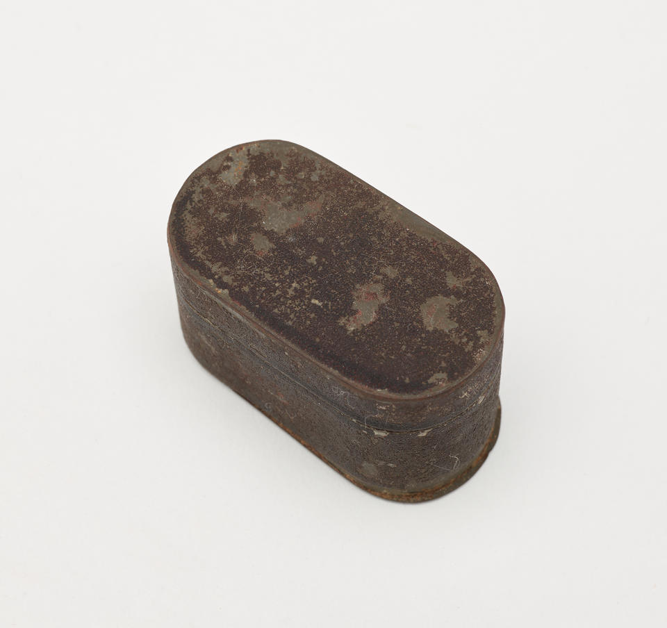 A tin and silver nutmeg grater, it has rounded corners and a shield on the lid. 