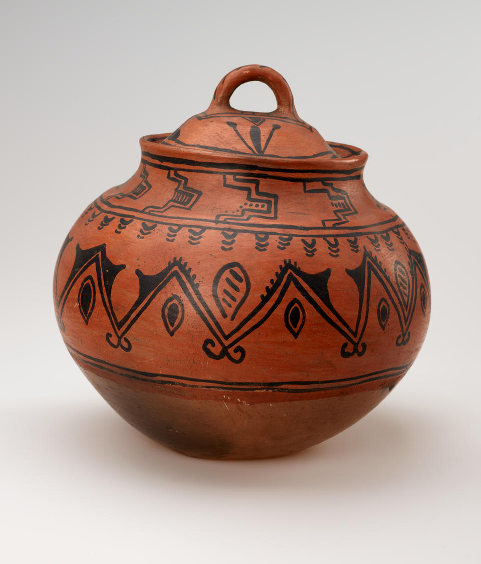 A bulbous red vessel with black abstract designs, leaning slightly to the right. The lid has a small round handle. 