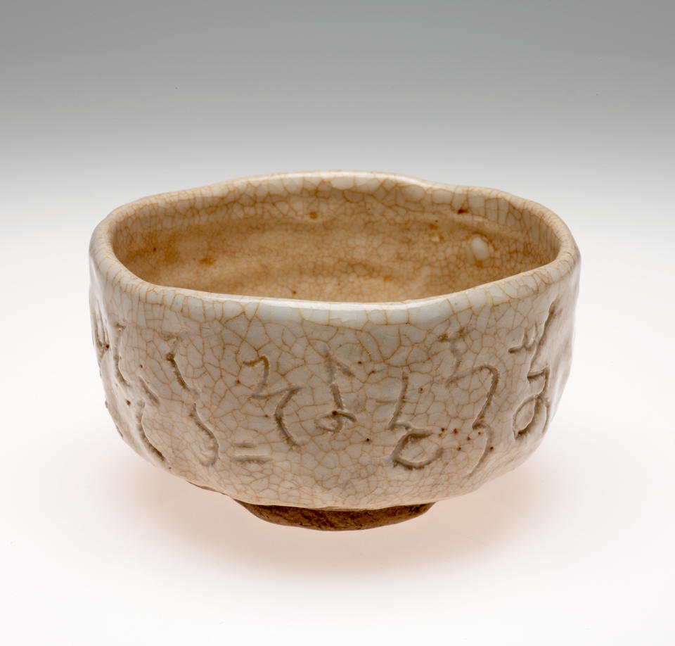 A bowl with undulating sides and rim. Cream and brown colored with a crackled surface and abstract designs scratched into the surface.