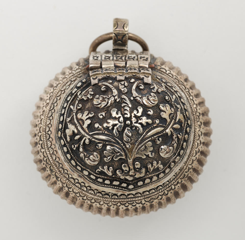 Rounded metal container with raised floral designs. A small circular metal ring attached to the top. 