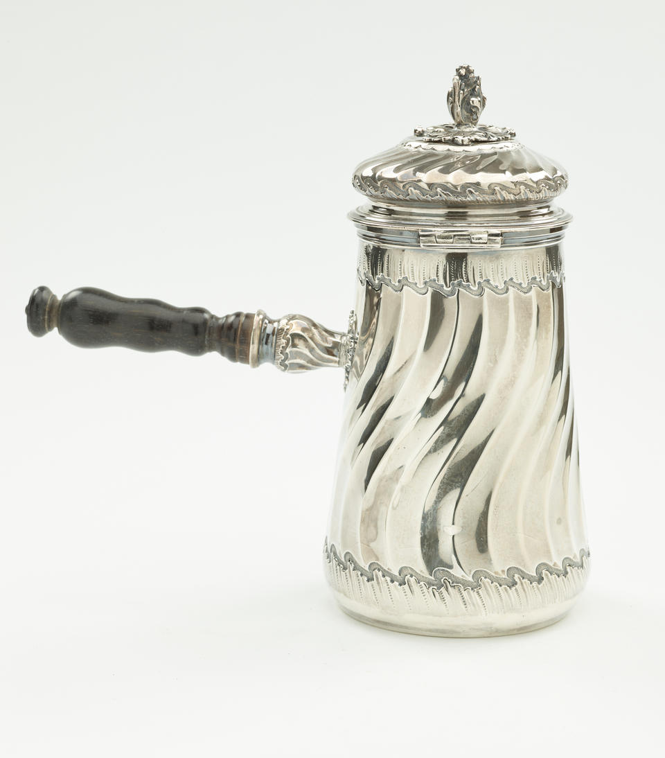 A silver chocolate pot with a decorative swirled body, lid, and fruit wood handle.