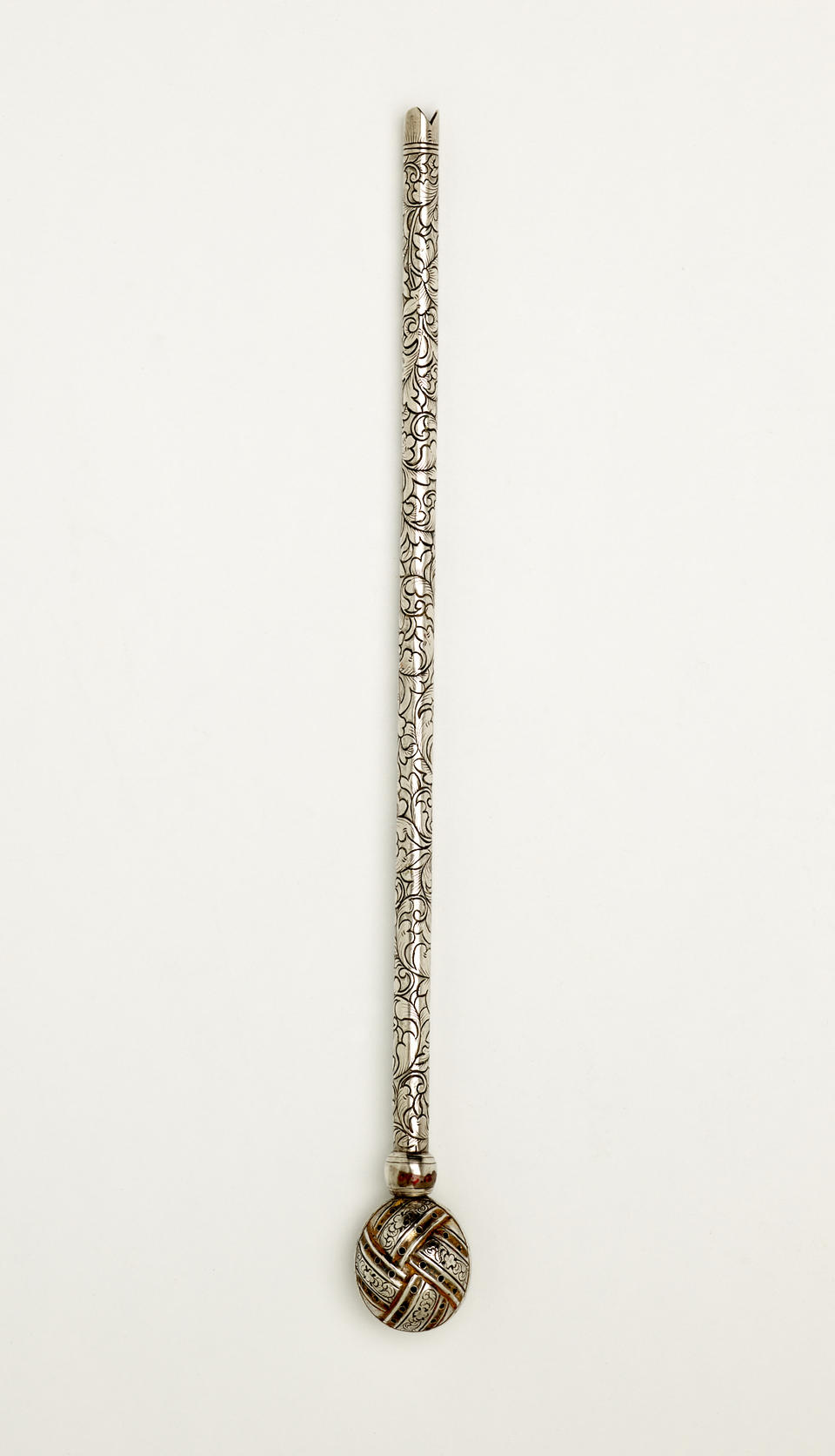 A long silver utensil used for tea with a decorative body and has one small bulbous end.