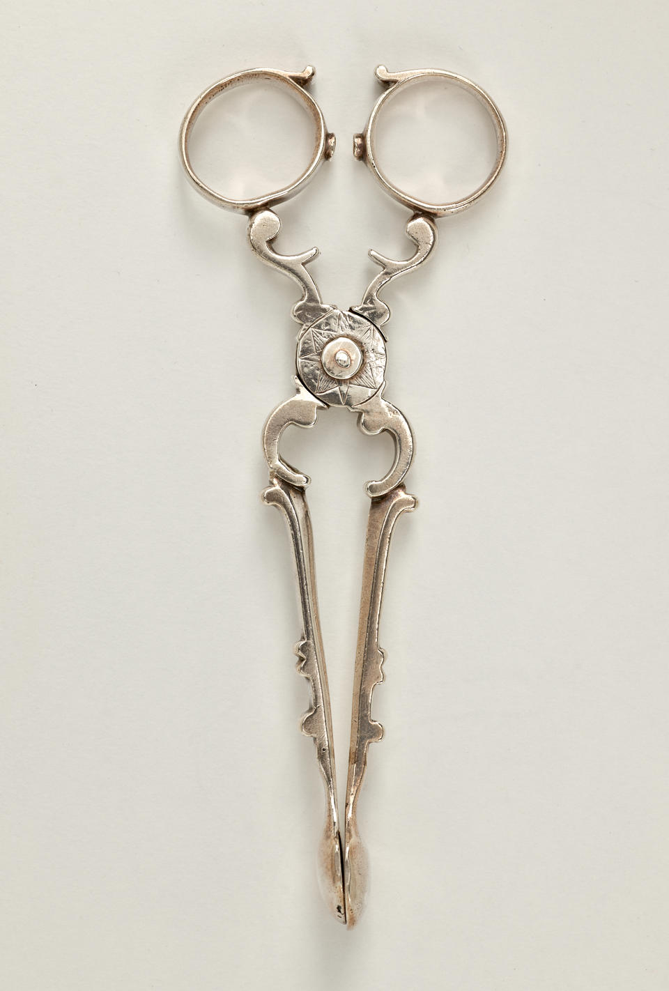 Silver sugar tongs that are delicate and swirled.