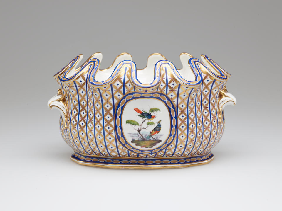 An open vessel with a deeply scalloped rim. A central decoration of two birds and a tree is surrounded by vertical bands of blue with gold diamond shapes. 