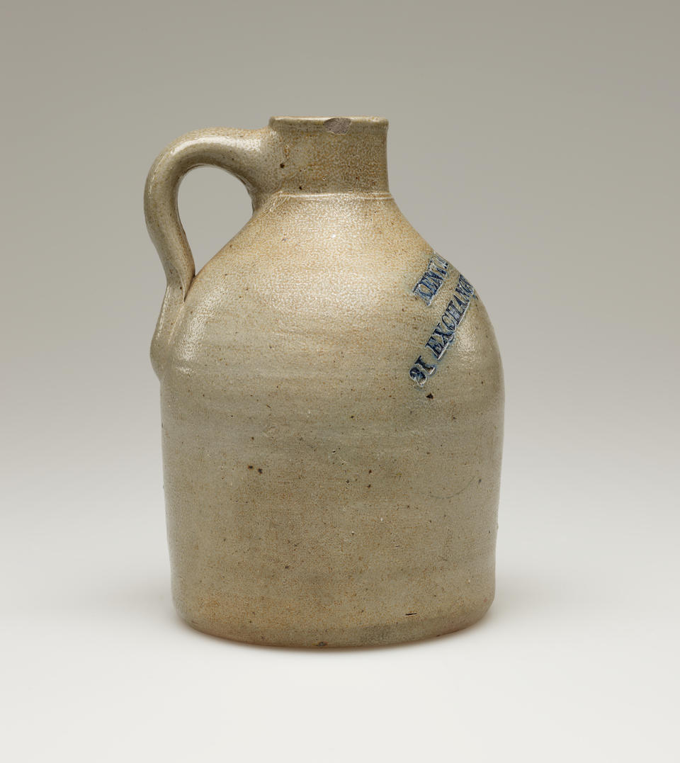 A round, sand colored jug with a small, rounded handle. Blue colored text  is stamped into the body of the jug, on the left side. Legible text reads, “PROV RI.”