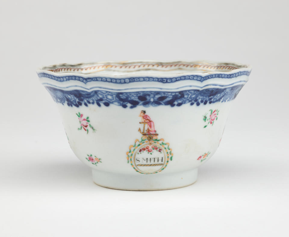 A porcelain sugar bowl with glided, blue, green, and pink decorations. The decorations are floral, as well as one figure, and a word saying “SMITH”.