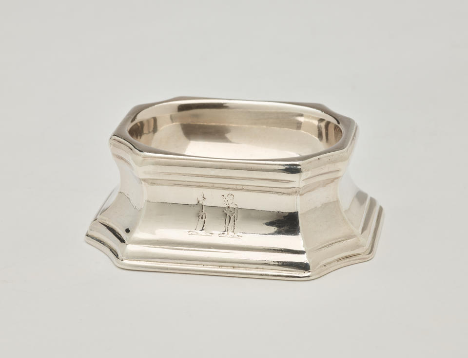 A silver salt container that is rounded on the inside and angular on the outside. 