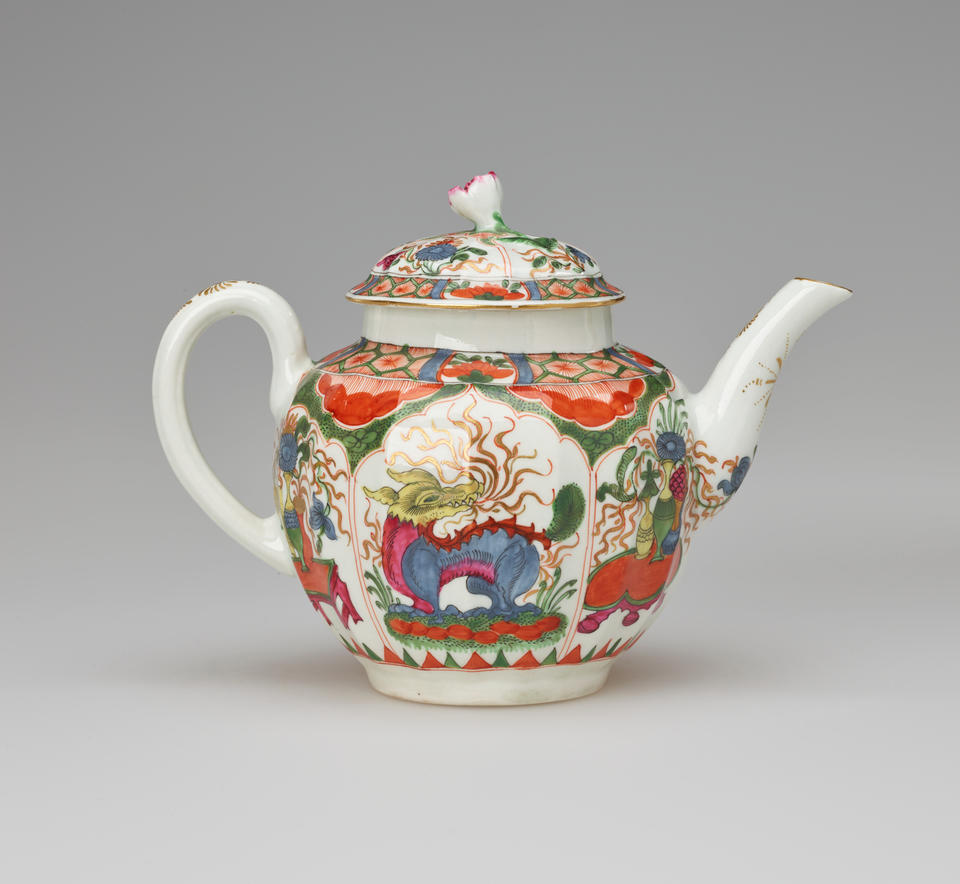 A white teapot with a handle, spout, lid and finial, with green, red, blue, pink, yellow and gilded decorations. The main vignite shows a dragon on a table.