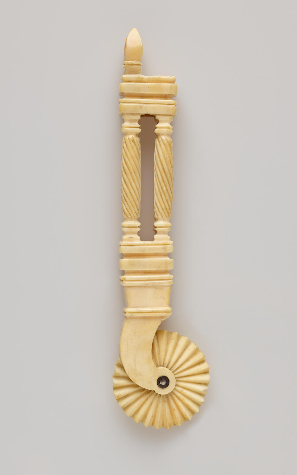 An ivory pie crimper with a decorative handle and a textured wheel. The handle has a cutout in the middle of it.