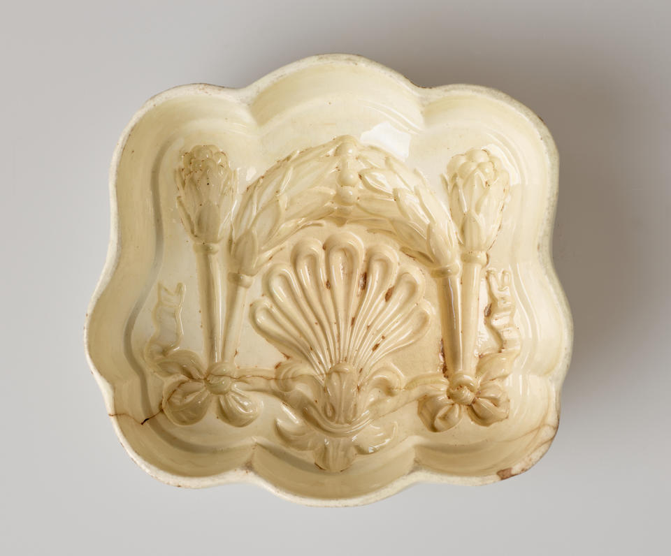 A ceramic pudding mould that is cream colored and is curved with inset floral and bow decorations.