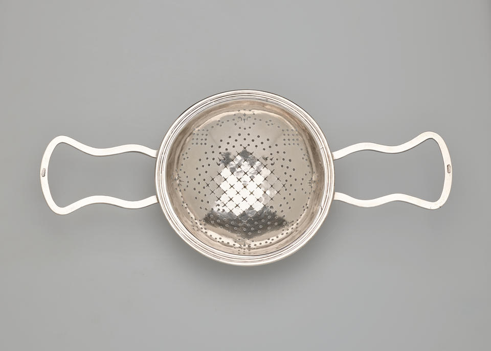 A round silver strainer with symmetrical undulating handles.