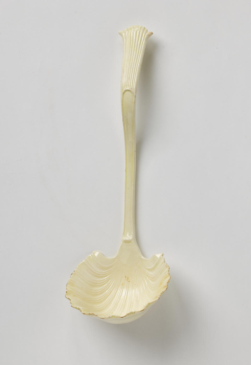A creamware ladle with a shell shaped bowl and simple necked handle that comes to a flared out point with linear decorations. 