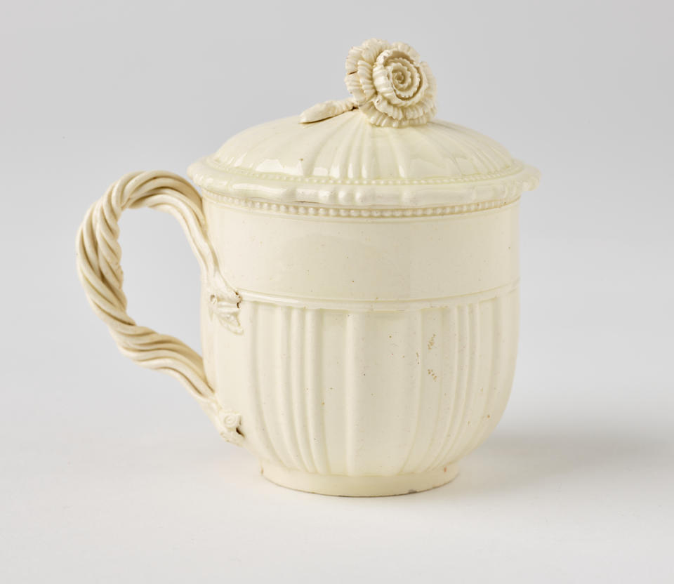 A white creamware custard cup, with a sculptural swirled handle, and lid with sculpted finial.
