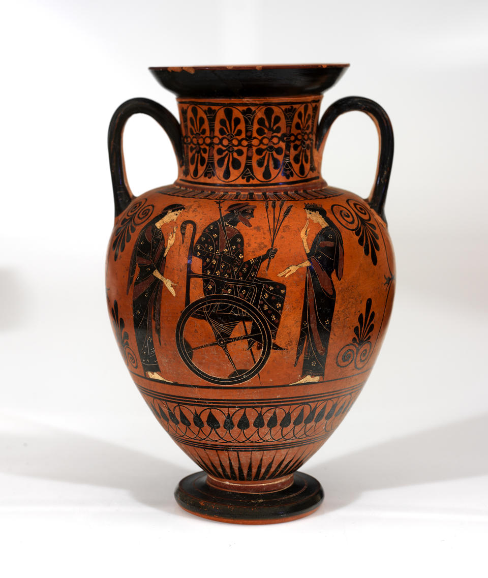 Orange clay jar with two handles. It is decorated with black patterns and an illustration of a man in a wheelchair holding a staff and grain, flanked by two women.