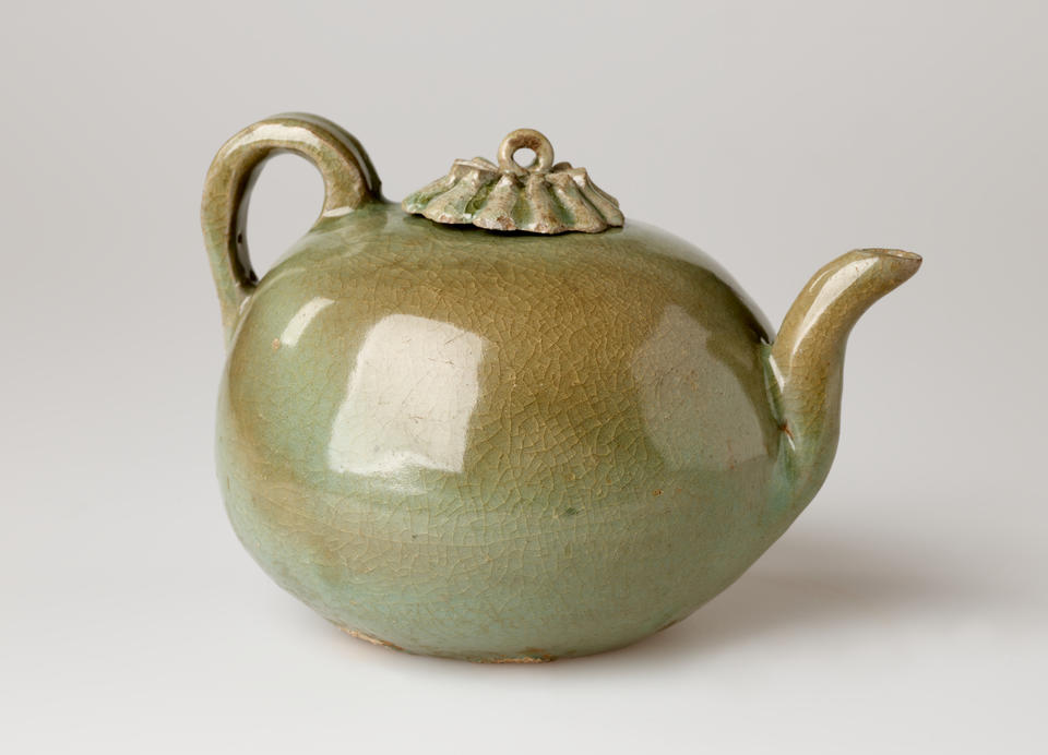 A rounded greenish brown water kettle with a handle, spout, and small decorative lid and a loop for a finial. 