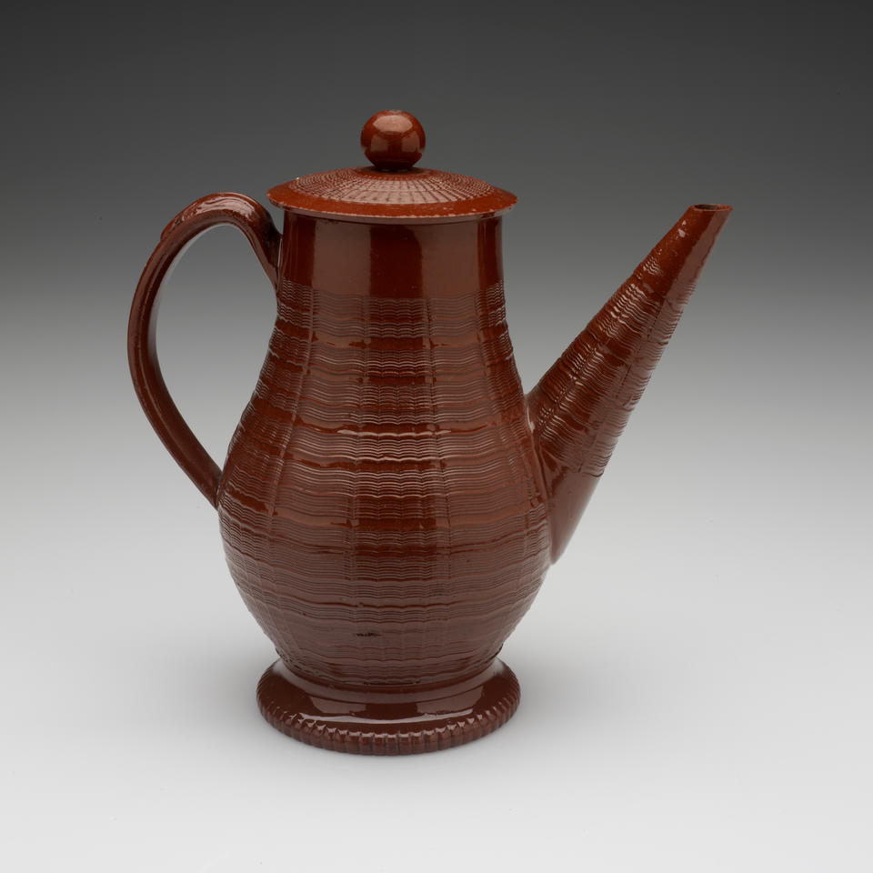 A brown stoneware coffee pot with a long straight spout, handle, foot, and lid with decorative horizontal grooves and projecting grooves. The final which is spherical in shape.