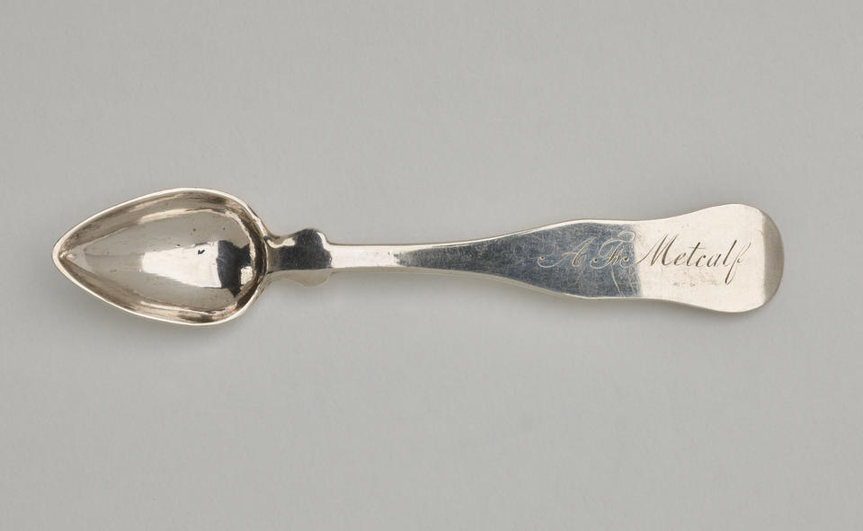  A silver salt spoon the bowl comes to a pointed tip, the neck is thin, and the handle is thicker and rounded at the end. 