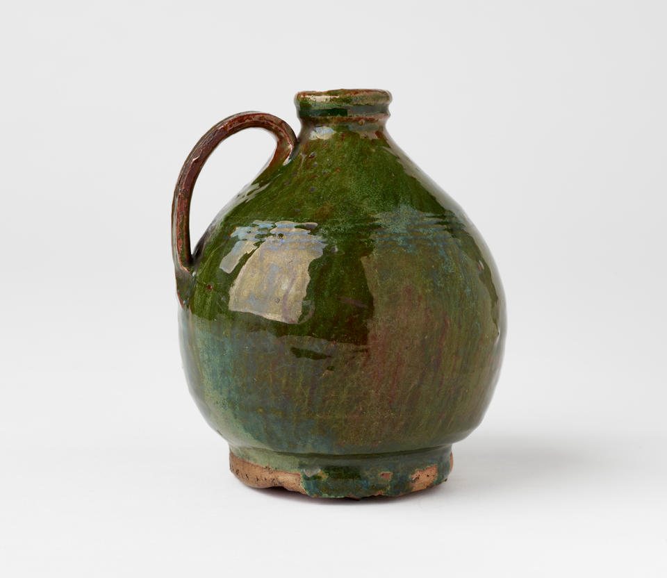 A short green bulbous jug with a tight rim, handle, and foot. 