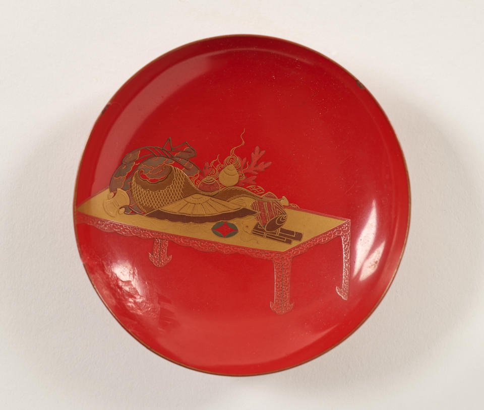 A lacquered wood wine cup that is bright red and has gold decorations. 
